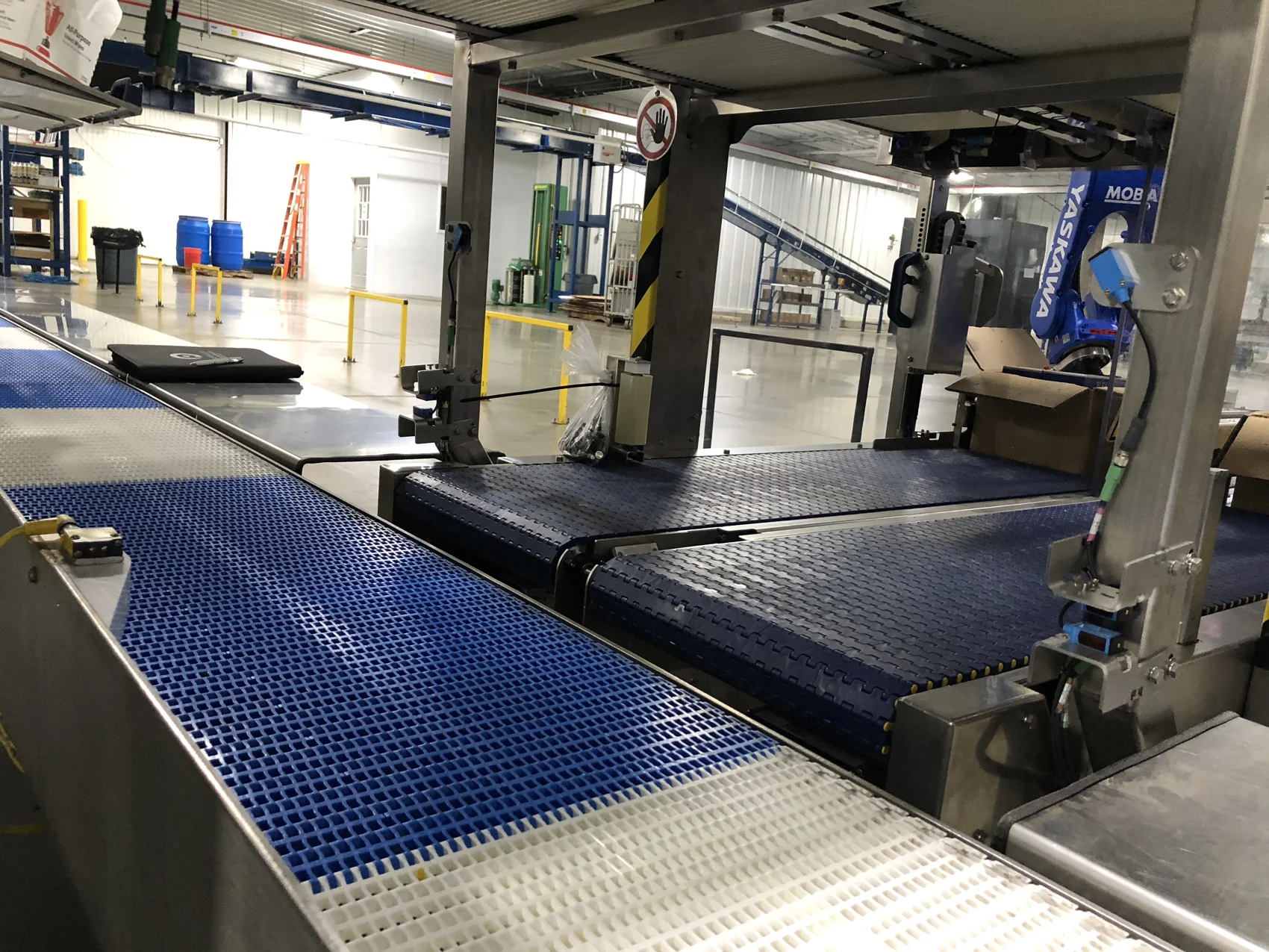 Modular plastic belt conveyors leading into a robotic packing cell in a food processing plant